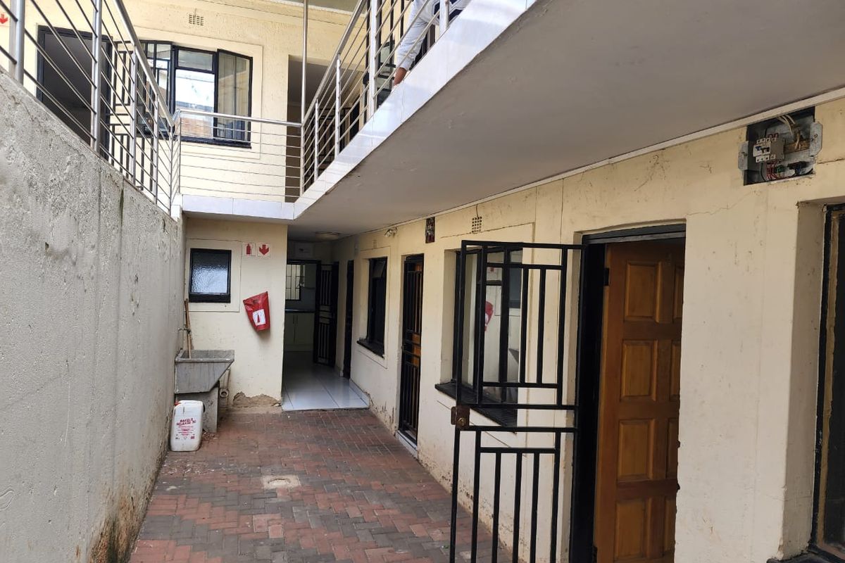 A paved rear courtyard area featuring a stainless steel balustrade, security gates, and an external utility sink, showing signs of wear and maintenance needs.