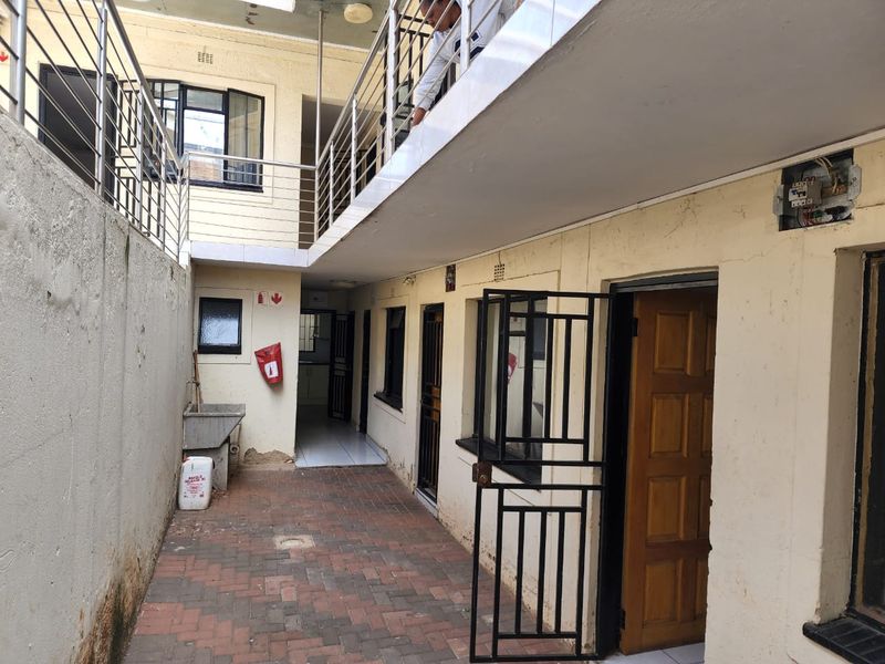 A paved rear courtyard area featuring a stainless steel balustrade, security gates, and an external utility sink, showing signs of wear and maintenance needs.