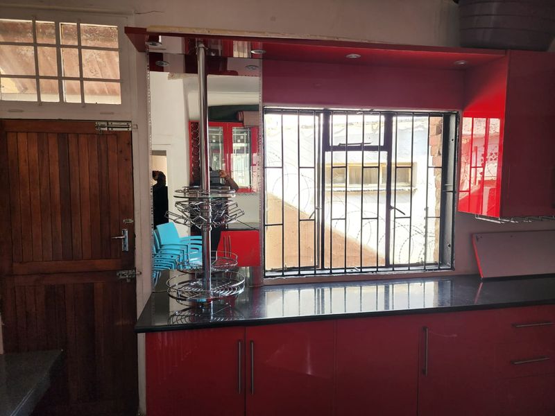 Kitchen area featuring high-gloss red cabinetry, granite countertops, and a timber door, with security bars installed on the window.