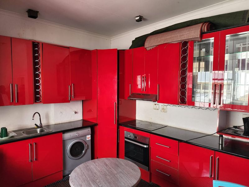 Kitchen featuring high-gloss red cabinetry, black granite countertops, built-in oven, cooktop, and integrated washing machine, requiring cosmetic updates to wall finishes.