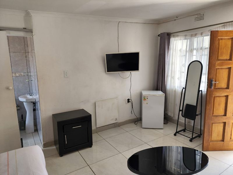 A bedroom featuring tiled flooring and an en-suite bathroom with a pedestal basin, requiring cosmetic updates to wall finishes and electrical tidying.