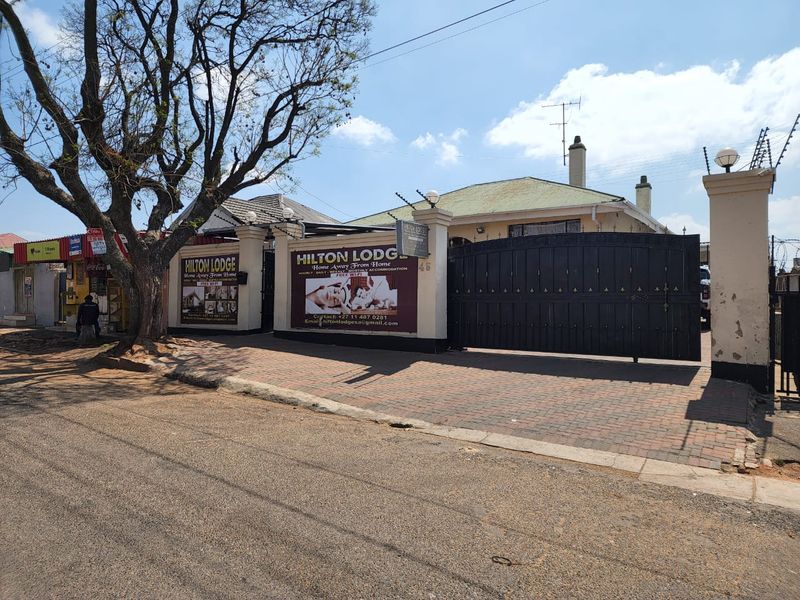 Front exterior view of the property featuring a paved driveway, secure perimeter wall with electric fencing, and a large sliding gate.