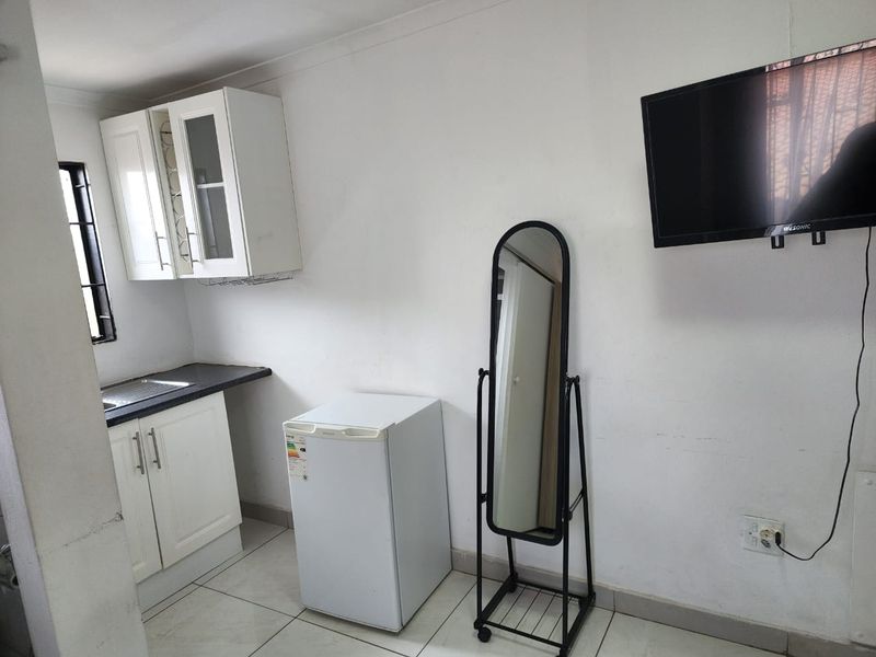 A compact kitchen area featuring white built-in cabinetry, a dark laminate countertop, a stainless steel sink, and tiled flooring.