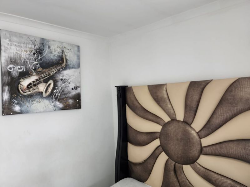 A close-up view of a bedroom corner featuring white walls with coving and a decorative headboard.