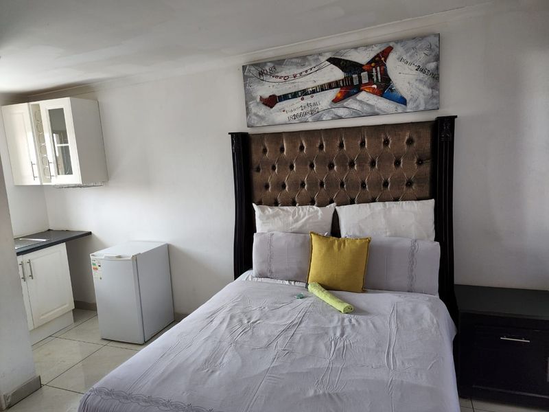 A bedroom featuring a kitchenette area with built-in cabinetry and tiled flooring, offering a compact living space.