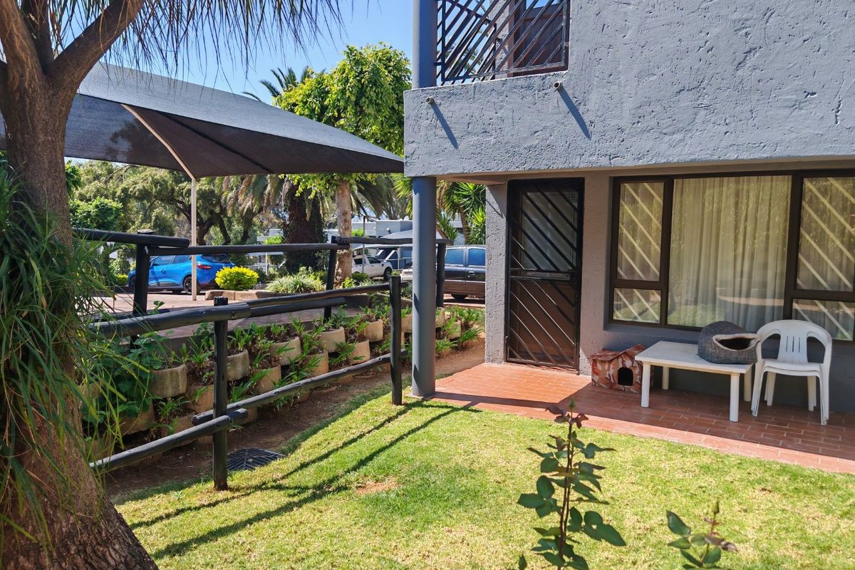 Rear exterior view of the townhouse featuring a small garden, a terracotta tiled patio area, and a balcony above.