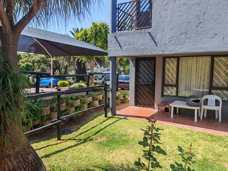 Rear exterior view of the townhouse featuring a small garden, a terracotta tiled patio area, and a balcony above.