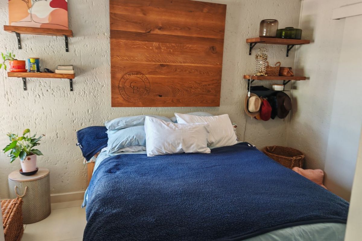 A cozy bedroom featuring textured walls, tiled flooring, and built-in wooden shelving units, providing a functional and rustic aesthetic.