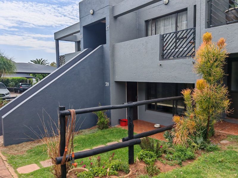 Front elevation of a townhouse unit featuring a ground floor patio, upper-level balcony with metal railings, and a private garden area.