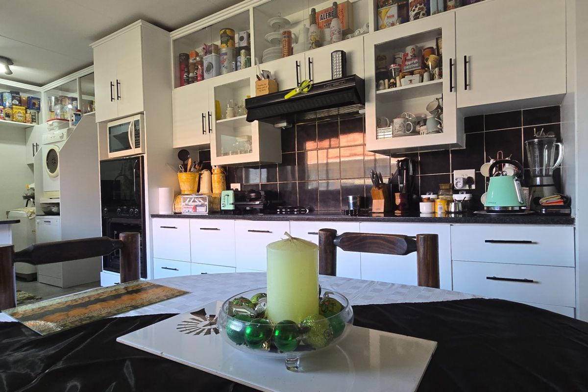 A functional kitchen featuring white cabinetry, dark tiled backsplash, built-in appliances, and an adjacent scullery area with additional storage and laundry facilities.