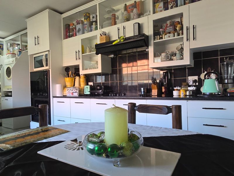 A functional kitchen featuring white cabinetry, dark tiled backsplash, built-in appliances, and an adjacent scullery area with additional storage and laundry facilities.