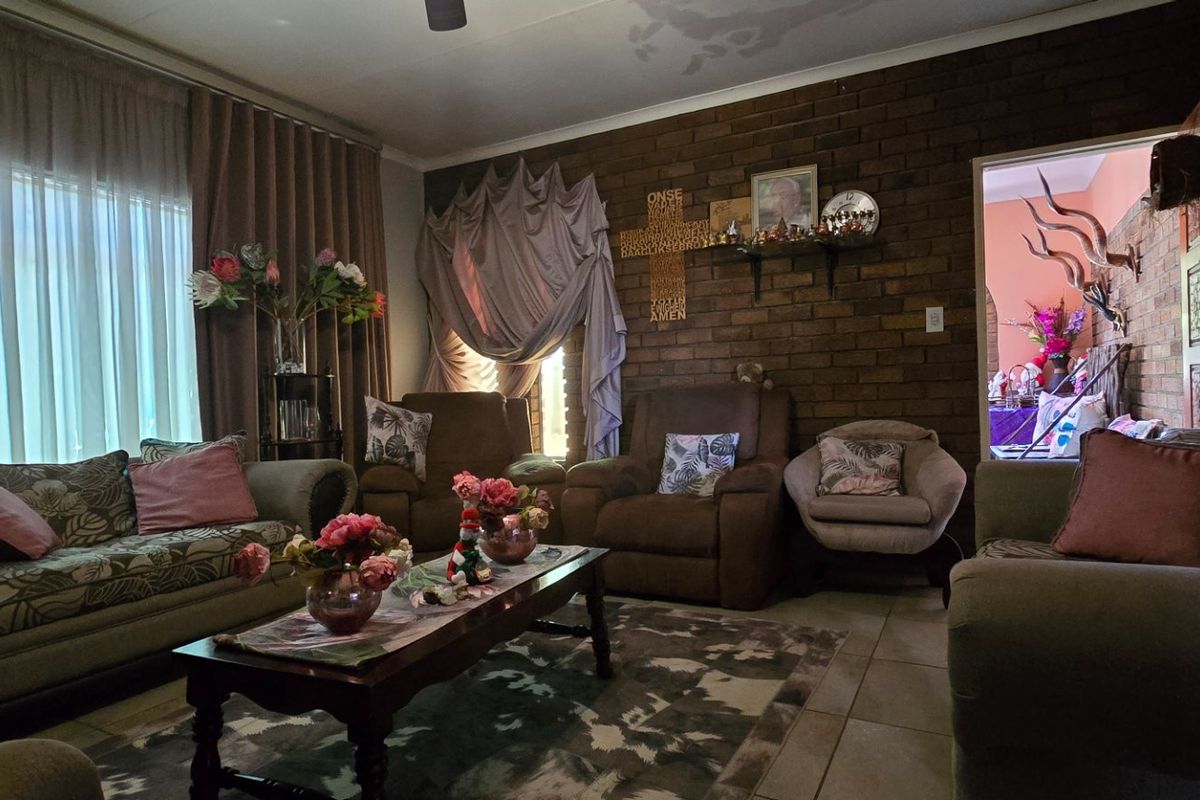 A cozy living room featuring an exposed brick feature wall, tiled flooring, and a ceiling fan, with visible signs of ceiling water staining.