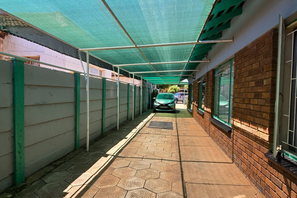A paved side exterior area featuring a shade cloth canopy, brick walling, and security bars on the windows.