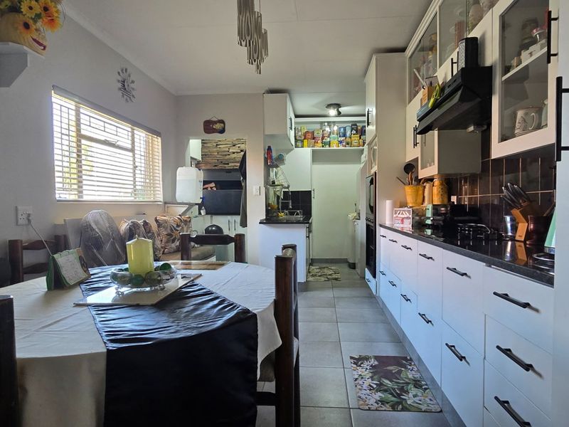 Open-plan kitchen and dining area featuring modern white cabinetry, black granite countertops, tiled flooring, and a built-in braai area.