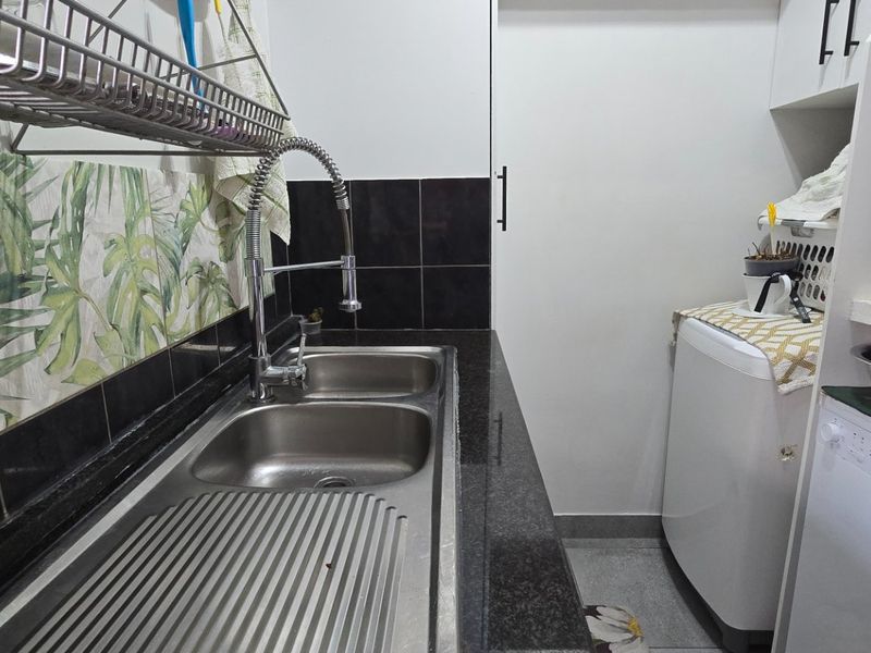 A functional laundry area featuring a double stainless steel sink, granite countertops, and tiled splashbacks with built-in cabinetry for storage.