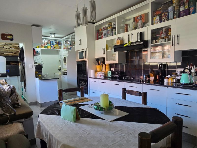 Open-plan kitchen and dining area featuring white cabinetry, granite countertops, built-in appliances, and a tiled backsplash, with an adjacent built-in seating area.