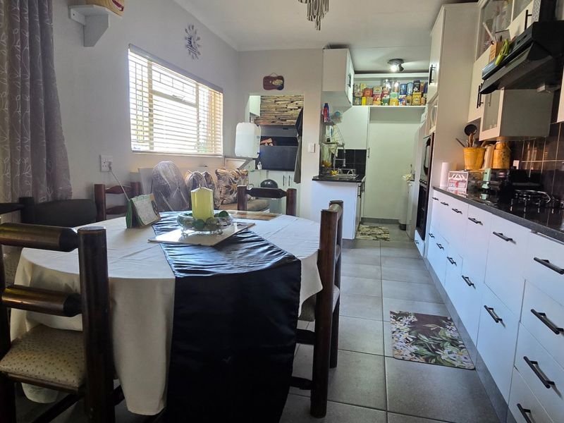 Open-plan kitchen and dining area featuring modern white cabinetry, tiled flooring, and a built-in braai area in the background.