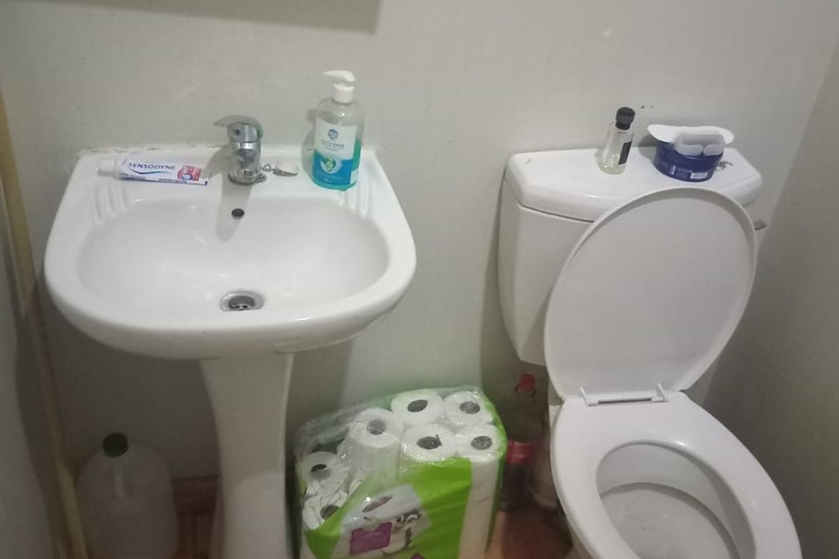 A compact bathroom featuring a white pedestal basin and standard toilet with laminate flooring.