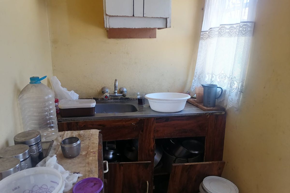 A small, dated kitchen area featuring a basic stainless steel sink, wall-mounted cabinetry, and base storage units in need of renovation.