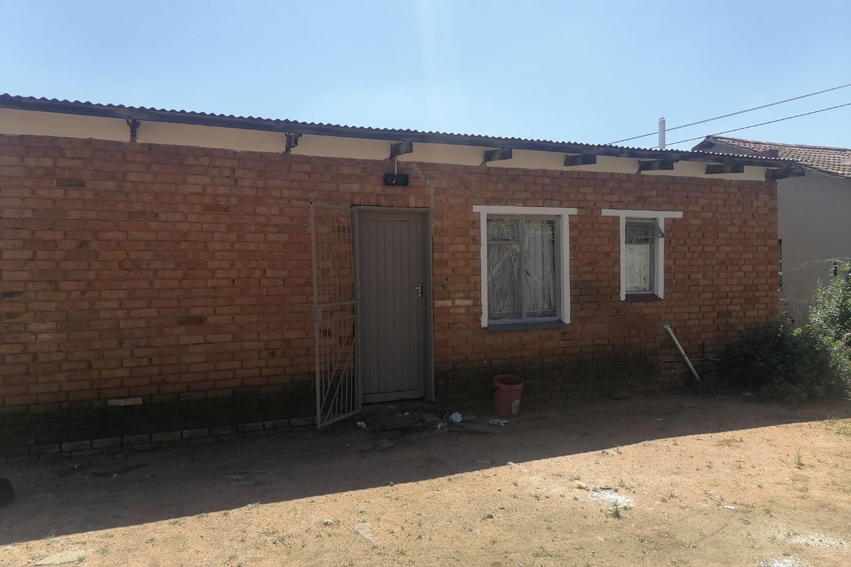 A single-story residential exterior featuring exposed brick walls, a corrugated metal roof, and steel-framed windows with an attached security gate.