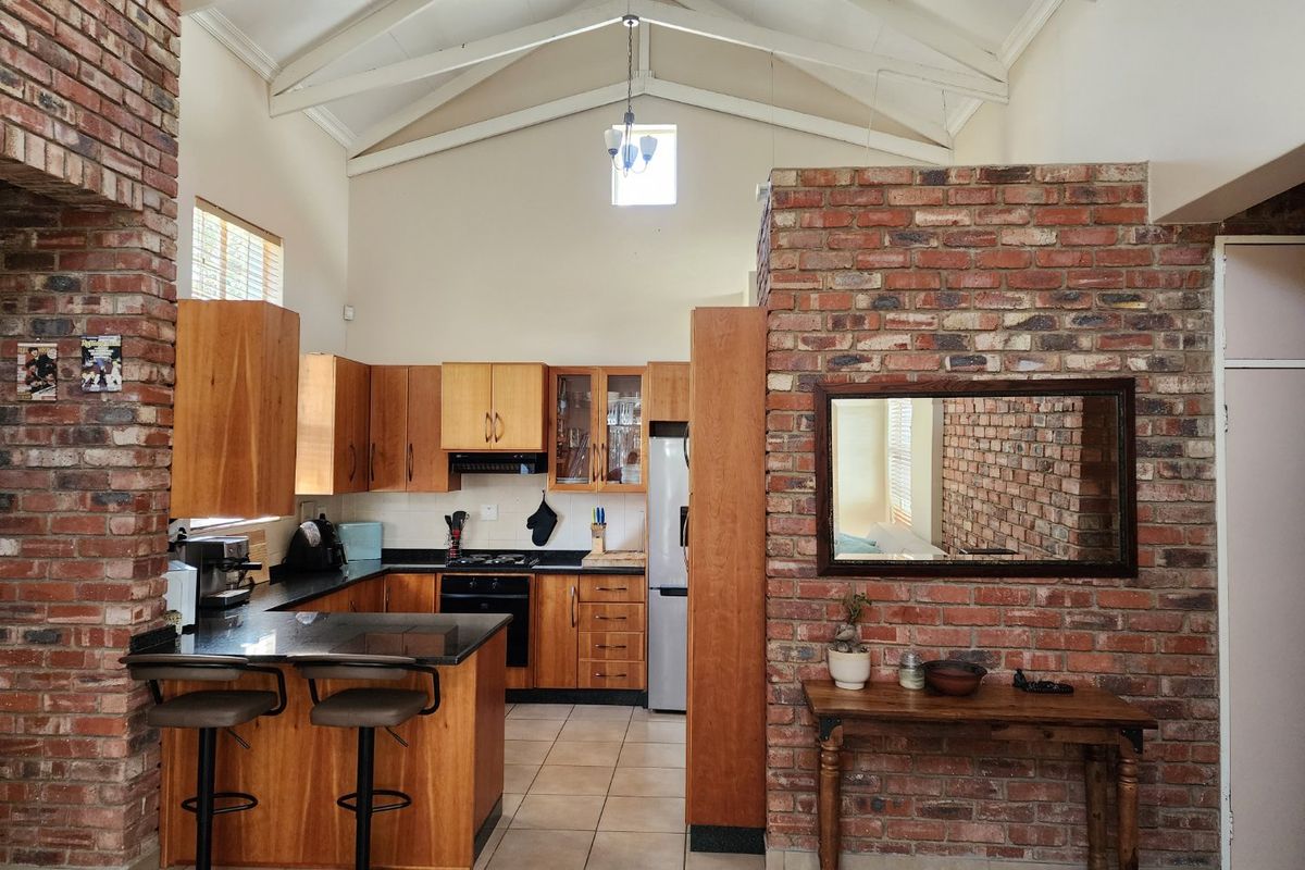 Spacious kitchen featuring vaulted ceilings, exposed brick accents, timber cabinetry, granite countertops, and integrated appliances, offering a warm and rustic aesthetic.