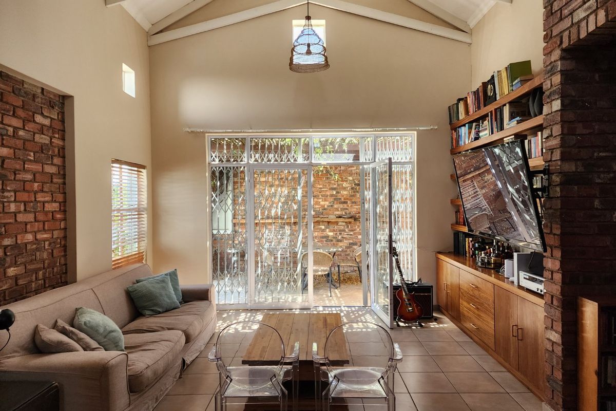Spacious living room featuring a vaulted ceiling, exposed brick accents, built-in cabinetry, and large glass doors opening to an outdoor patio area.