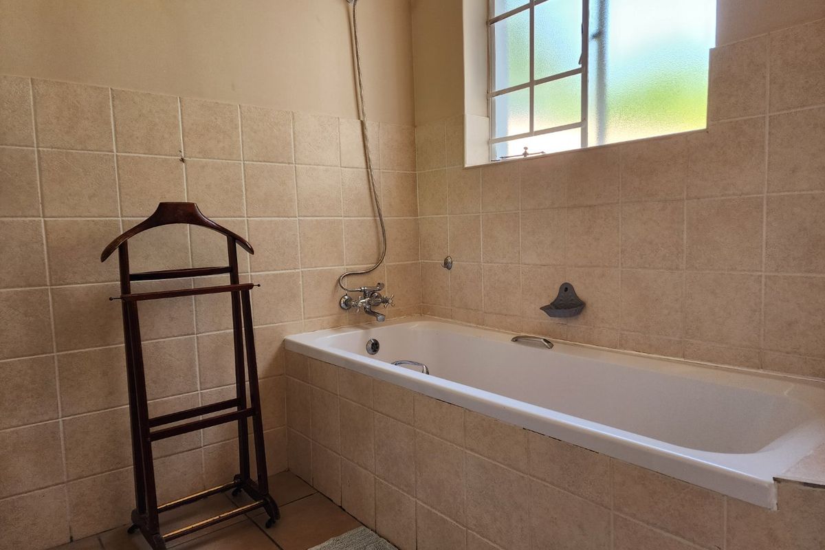 A functional bathroom featuring a built-in bathtub with wall-mounted shower fixtures, tiled walls, and a frosted glass window for natural light.