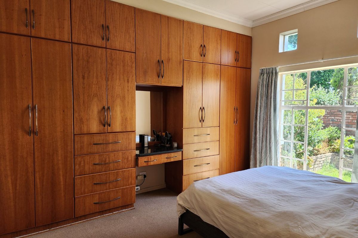A bedroom featuring extensive floor-to-ceiling built-in wooden cabinetry with an integrated vanity station, carpeted flooring, and natural light from a large window.