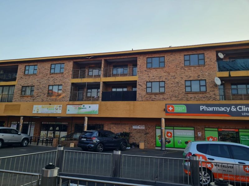 Exterior view of a multi-story apartment building featuring face brick facade, private balconies with stainless steel railings, and ground-floor commercial retail spaces.