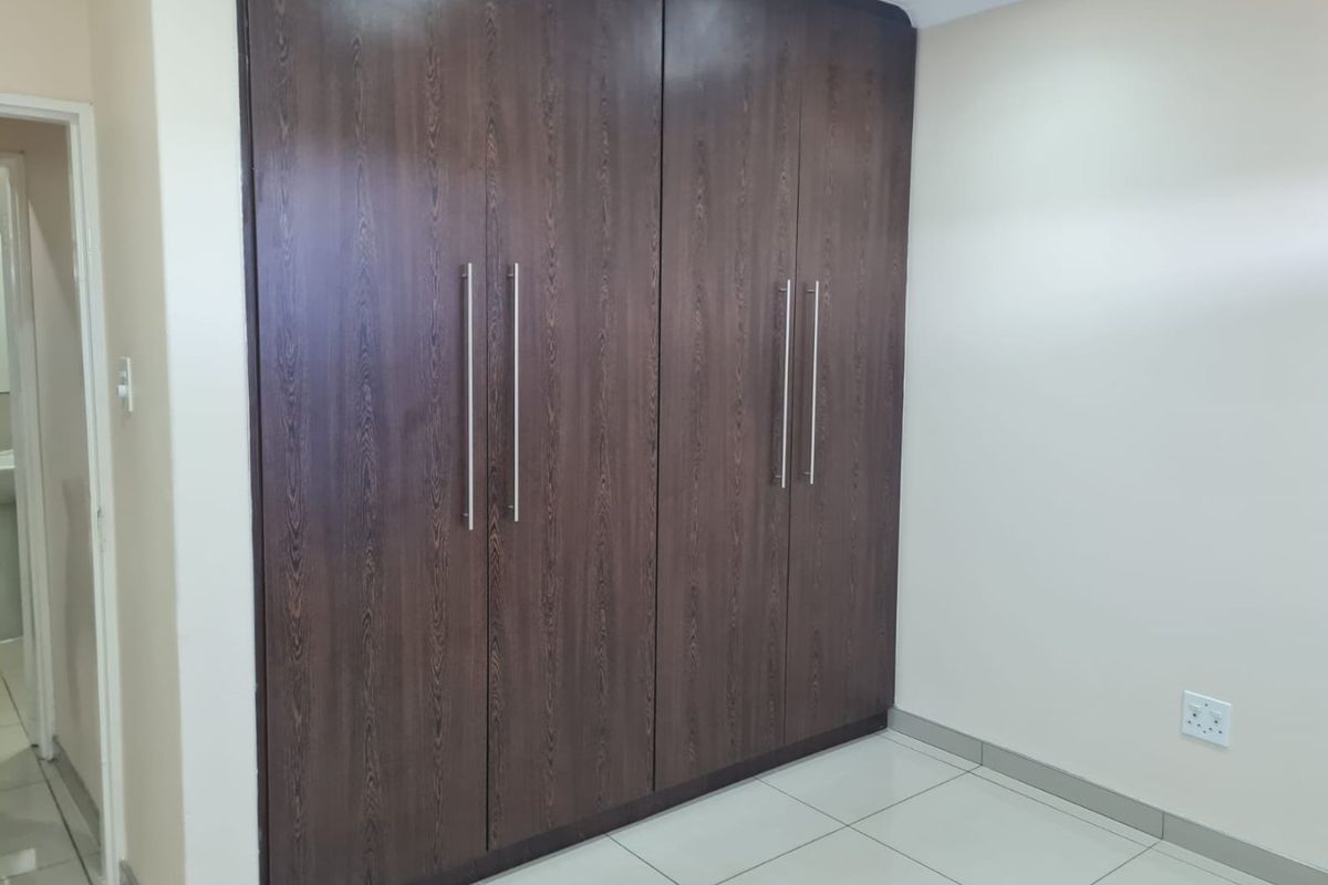 A clean, empty bedroom featuring modern dark wood built-in cupboards and neutral tiled flooring, offering a versatile space ready for personalization.
