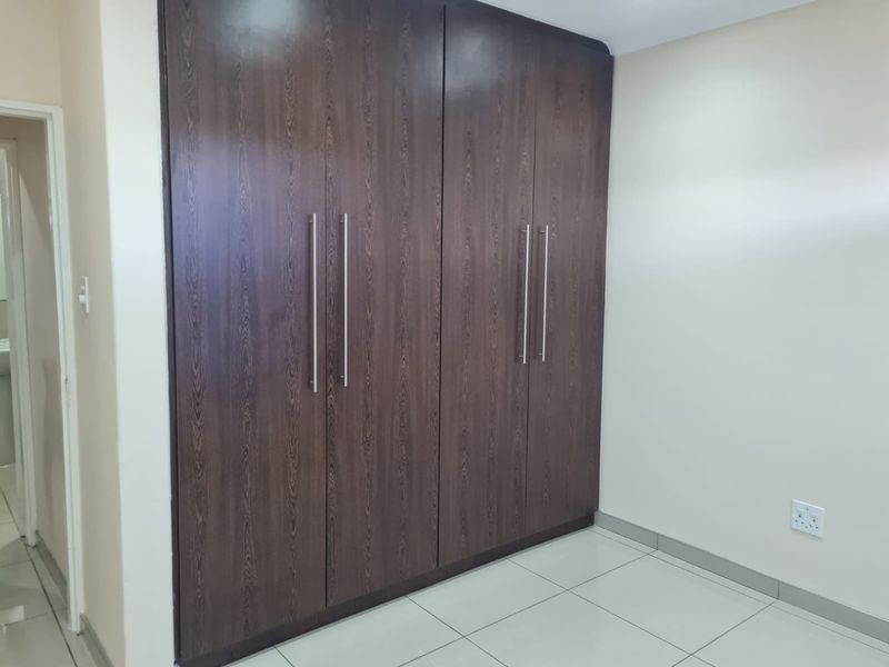 A clean, empty bedroom featuring modern dark wood built-in cupboards and neutral tiled flooring, offering a versatile space ready for personalization.