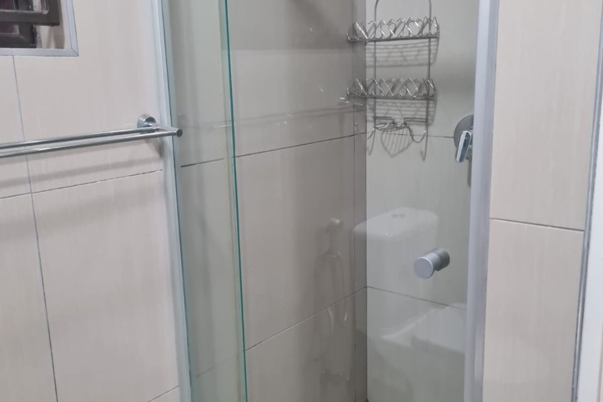 A clean, modern bathroom shower enclosure featuring neutral wall tiles, a glass door, and a tiled floor.