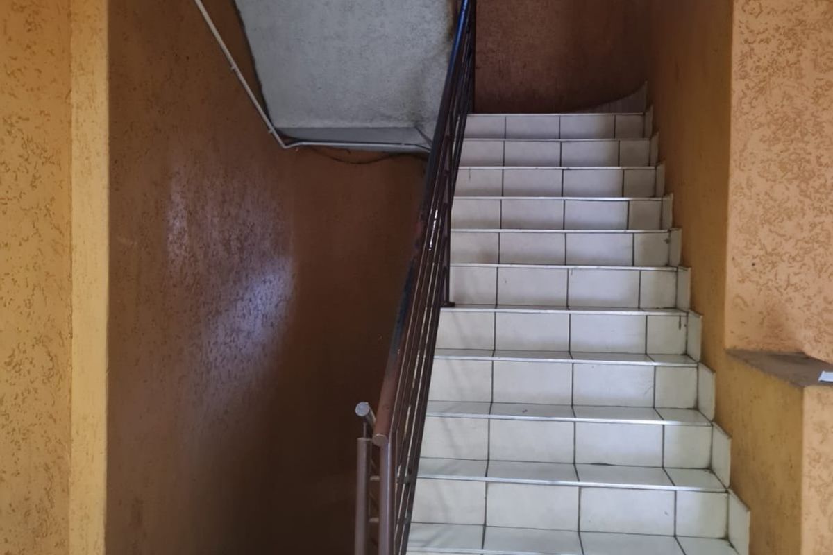 A communal stairwell featuring tiled steps, a metal handrail, and textured walls, currently showing signs of wear and maintenance requirements.
