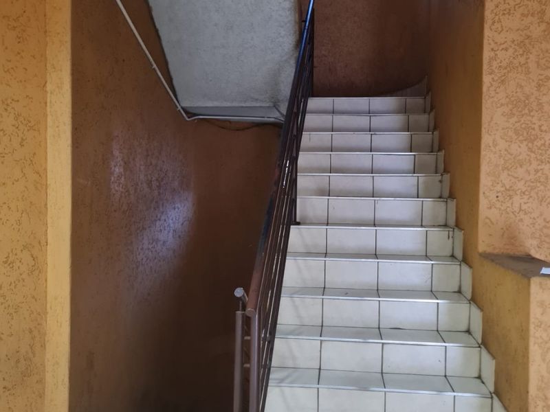 A communal stairwell featuring tiled steps, a metal handrail, and textured walls, currently showing signs of wear and maintenance requirements.