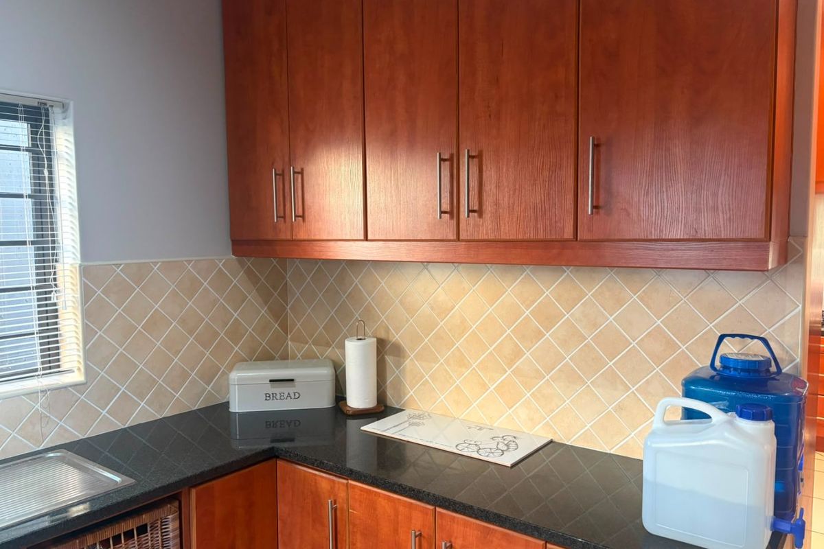 A functional kitchen area featuring warm-toned wooden cabinetry, dark granite countertops, and a classic diamond-patterned tiled backsplash.