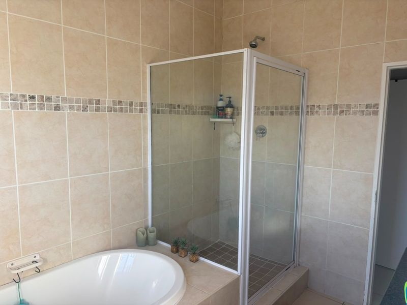 A functional bathroom featuring a built-in bathtub and a separate glass-enclosed shower with neutral wall tiling.