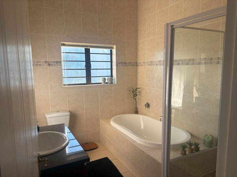 A functional bathroom featuring a built-in bathtub, separate glass shower enclosure, vanity basin, and neutral wall tiling.