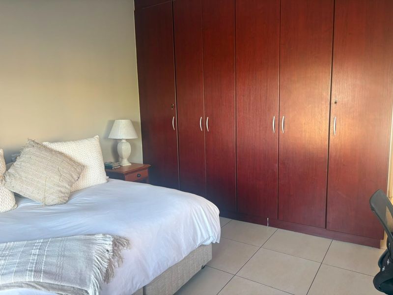 A bedroom featuring large, dark wood-finish built-in cupboards and neutral tiled flooring, offering ample storage space.