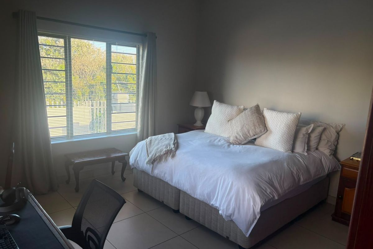 A spacious bedroom featuring neutral tiled flooring and a large window with venetian blinds, providing ample natural light.