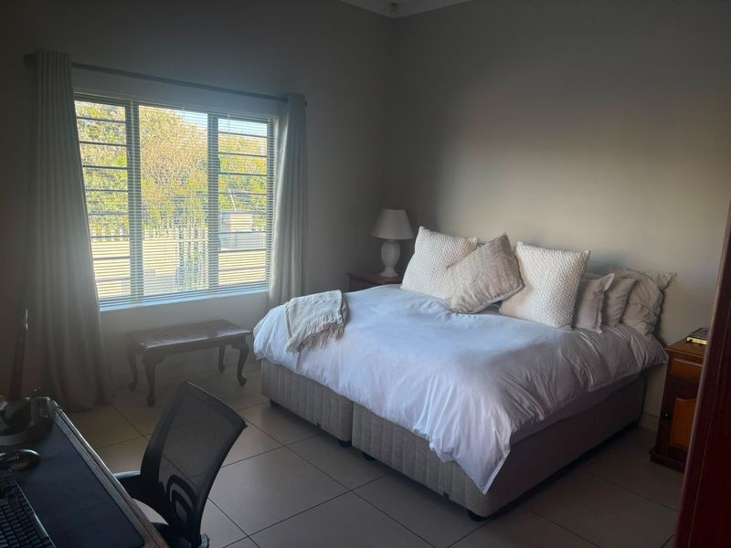A spacious bedroom featuring neutral tiled flooring and a large window with venetian blinds, providing ample natural light.