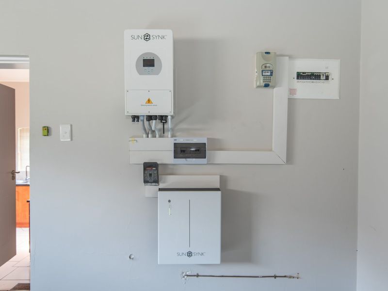 A clean utility wall featuring a modern Sunsynk solar inverter and battery storage system alongside the main electrical distribution board and prepaid meter.