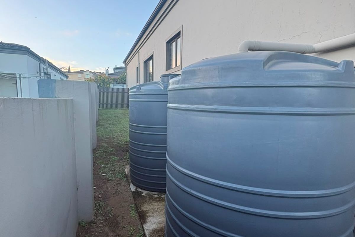 Side yard area featuring two large water storage tanks installed against the exterior wall of the property.