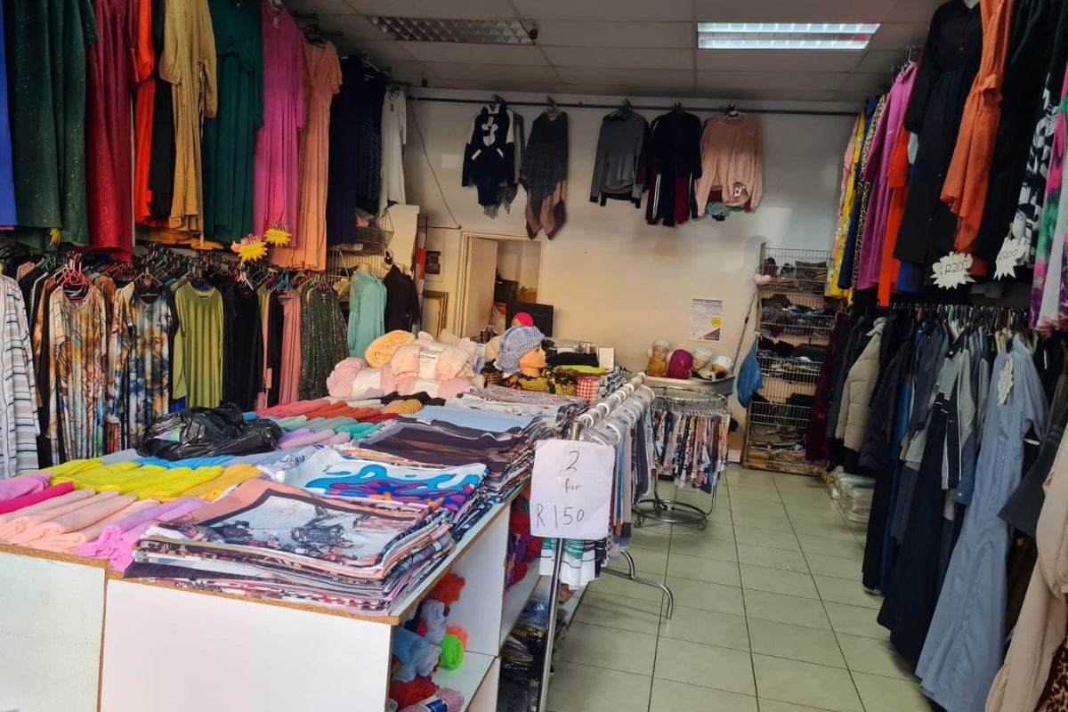 Commercial retail space featuring suspended ceiling tiles, fluorescent lighting, and tiled flooring, currently utilized for clothing sales.