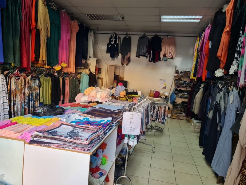 Commercial retail space featuring suspended ceiling tiles, fluorescent lighting, and tiled flooring, currently utilized for clothing sales.