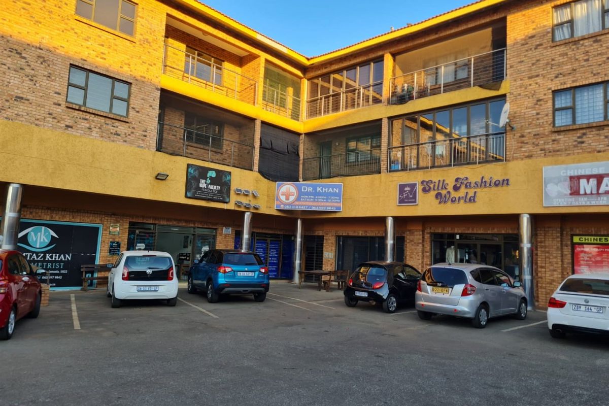 Front view of a multi-story commercial building featuring brick facade, multiple storefronts, and a paved parking area for customers.
