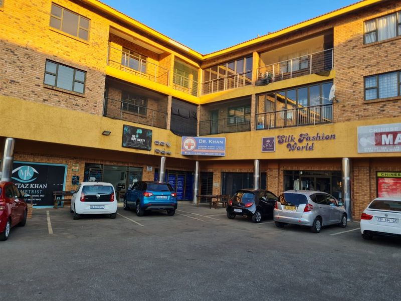 Front view of a multi-story commercial building featuring brick facade, multiple storefronts, and a paved parking area for customers.