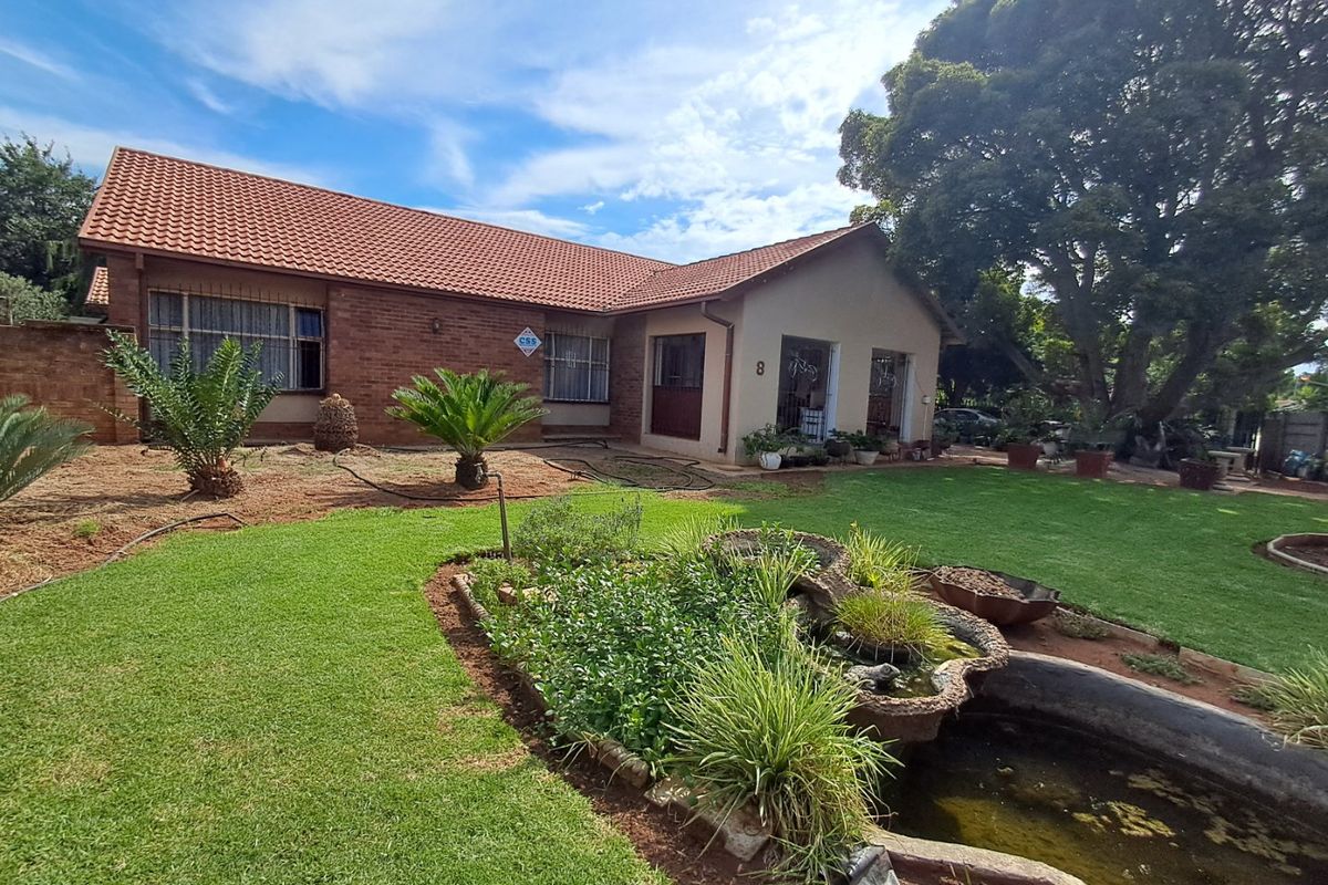 Rear view of a brick house featuring a tiled roof, security bars on windows, and a large garden with a built-in water feature.