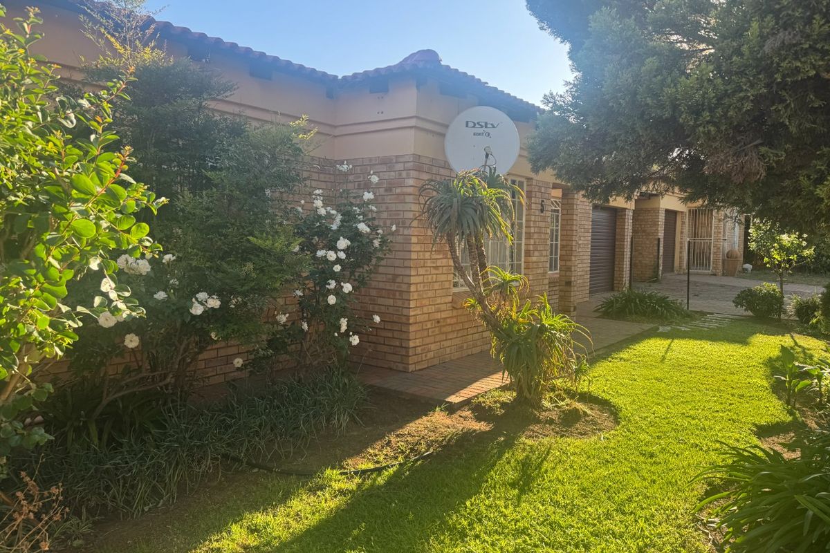 Front exterior view of a face brick townhouse featuring a tiled roof, paved driveway, and established garden area.