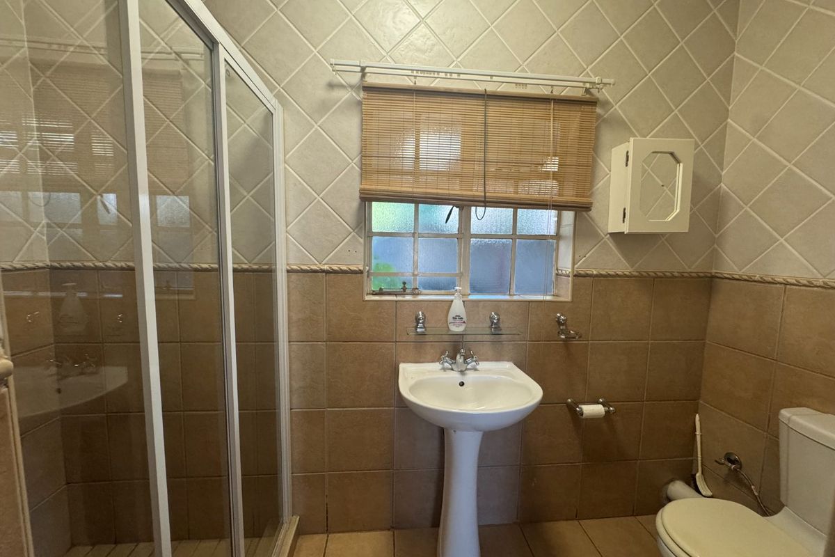 A functional bathroom featuring a pedestal basin, shower enclosure, and toilet with classic tiled finishes.