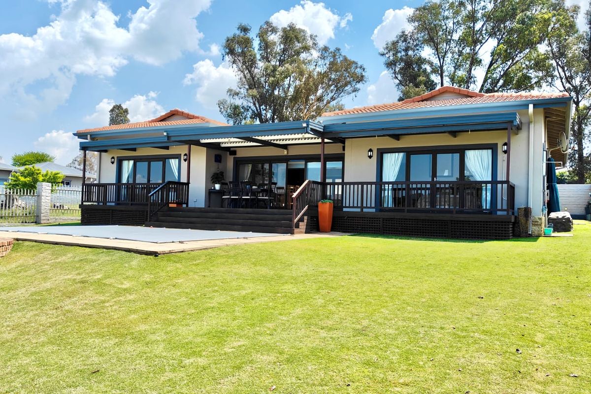 Rear view of the house featuring a spacious lawn, a raised timber deck with sliding door access, and a swimming pool with a cover.